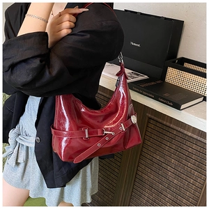 Close-up of deep red glossy underarm bag with silver buckle and decorative strap