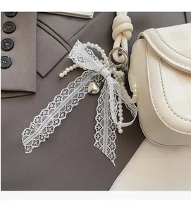 Detail of elegant lace bow with faux pearls and silver heart pendant on a shoulder bag