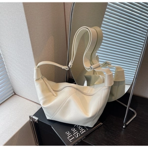 Detail of a minimalist cream shoulder bag featuring asymmetrical folds and metal zipper