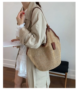 Detail of the woven straw tote bag featuring brown leather trim and long shoulder straps