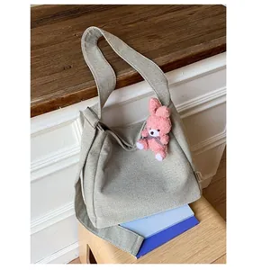 Detail of gray canvas tote bag featuring a pink plush rabbit charm and wide strap