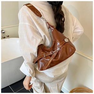 Rear view of model wearing glossy brown patent leather hobo bag with wide shoulder strap