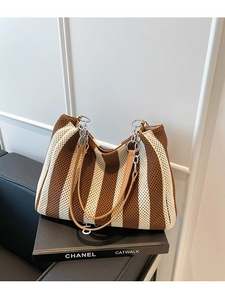 Striped woven tote bag with brown leather handles and silver chain on a decorative book
