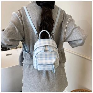 Détail du mini sac à dos à carreaux bleu clair porté par un mannequin dans un décor épuré
