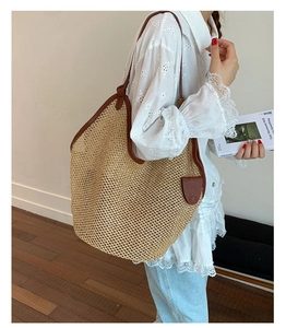 Side view of large straw tote bag with brown leather trim carried by a model