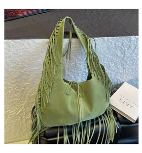 Detail of green suede hobo bag with long tassels and woven edges on artistic background