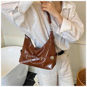 Detail of glossy brown leather crescent shoulder bag featuring adjustable strap and buckle