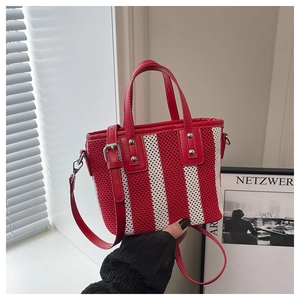 Détail d'un sac cabas en maille tissée rouge et blanc avec des anses en cuir et clous
