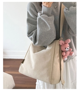 Detail of canvas tote bag with a pink plush bunny charm and wide shoulder strap
