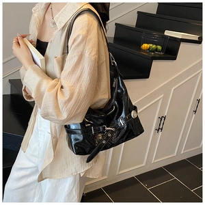 Detail of glossy black moon shoulder bag with silver buckles and decorative strap on model