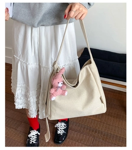 Detail of beige canvas hobo bag with wide shoulder strap and pink plush bear pendant