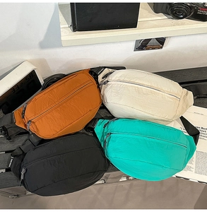 Stack of nylon cross-body bags in orange, cream, black, and green on a shelf
