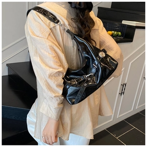 Close-up of black patent leather shoulder bag with silver eyelet straps and crescent shape