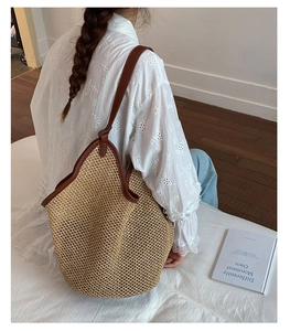 Detail of large woven beach tote showing straw texture and brown leather strap handles