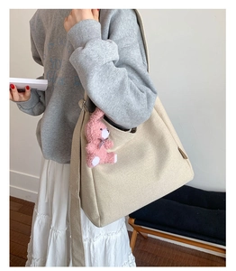 Detail view of large beige canvas tote bag with a pink plush bear charm and wide strap