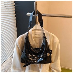 Detail of black glossy patent leather shoulder bag with wide strap on white blazer