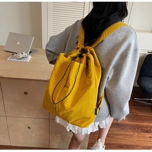 Mustard yellow drawstring backpack shown from a side view on a model for casual travel