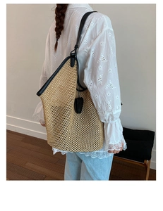 Detail of woven straw tote bag with black leather straps and heart-shaped pendant detail