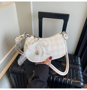 Détail d'un sac à carreaux avec nœud en dentelle, chaîne en perles et breloque cœur