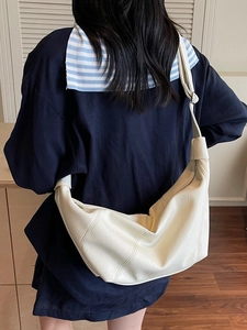 White pleated dumpling crossbody bag with adjustable wide strap shown on a model