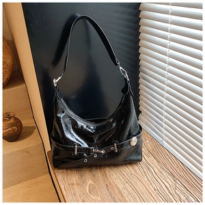 Detail of glossy black leather hobo bag with silver buckle on a wooden surface