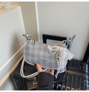 Détail du sac bandoulière argenté à carreaux avec breloque en perles et logo gravé