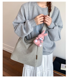 Detail of grey canvas tote bag with wide strap and a cute pink plush bunny charm