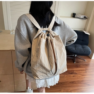 Rear view of a minimalist beige drawstring backpack with textured fabric in a home setting