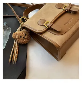 Detail of retro brown leather crossbody bag featuring metal buckles and plush bear charm