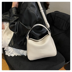 Detailed macro view of the cream lychee-textured leather and metallic hardware of the handbag