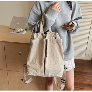 Detail of beige drawstring backpack showing front pockets and nylon fabric texture