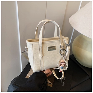 Borsa a tracolla bianco crema con motivo litchi e ciondolo a perla in un ambiente interno