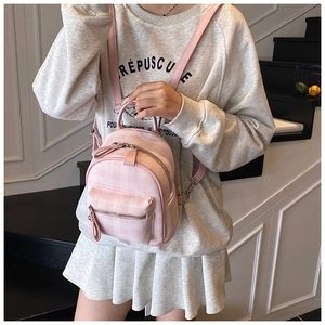 Gros plan du mini sac à dos à carreaux roses avec zips argentés porté par un mannequin
