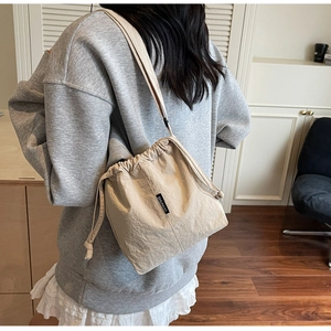 Detail view of beige nylon drawstring bucket bag showing side brand label and soft fabric texture