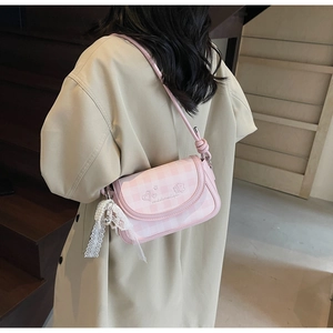 Pink checkered crossbody bag with lace bow and pearl charm detail worn by a model