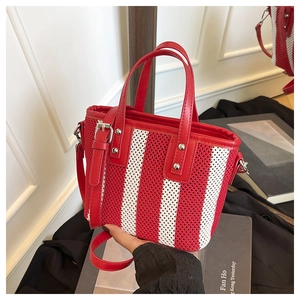 Détail du sac seau tissé à rayures rouges et blanches avec poignées en cuir et garnitures en métal