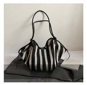Close-up of black and white striped woven tote bag with premium leather handles on a suit