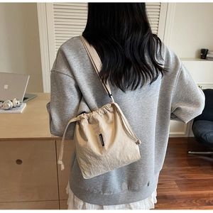 Macro detail of beige drawstring bucket bag showing canvas texture and brand tag