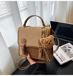 Detail of a brown patchwork leather bag with decorative straps and a plush bear charm