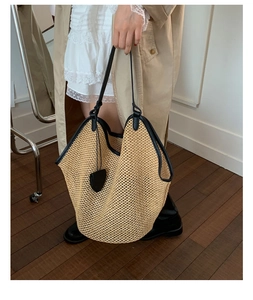 Close-up of a woven straw tote bag featuring black leather trim and heart charm detail