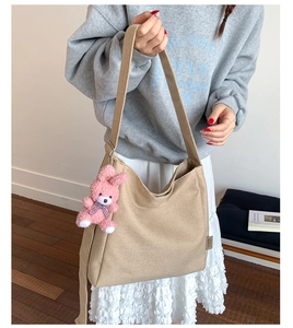 Detail of khaki canvas hobo bag featuring wide shoulder strap and pink plush bunny charm