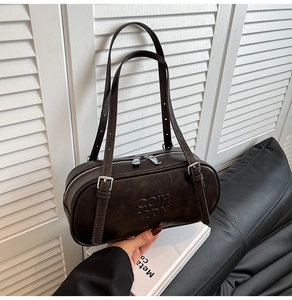 Detail of dark brown leather cylinder bag featuring embossed letters and double zipper