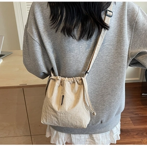Detail of off-white drawstring crossbody bag with side woven label and nylon texture