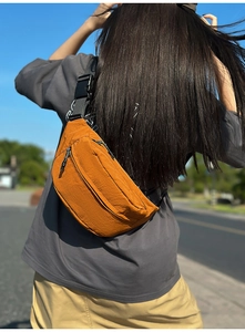 Detail view of the orange crossbody bag showing the wrinkled tech fabric and zip closures
