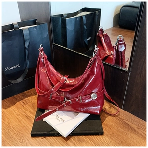 Close-up of bright red patent leather shoulder bag with silver buckle and logo detail