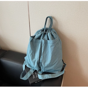 Close-up of light blue nylon drawstring backpack on a black leather sofa with book