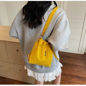 Detail of a bright yellow drawstring bucket bag worn over the shoulder in a cozy setting
