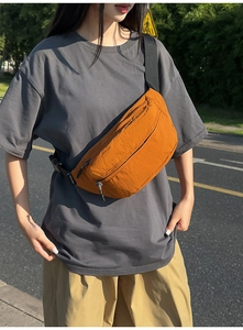 Detail of ginger orange nylon chest bag with wrinkled texture and brand woven label