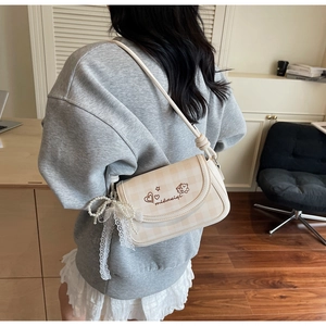 Close-up of cream plaid crossbody bag featuring bear embroidery and pearl lace charm