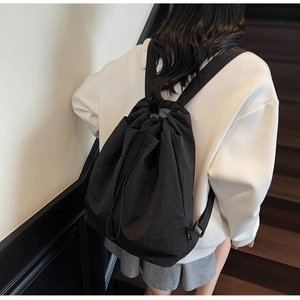Close-up of minimalist black nylon drawstring backpack worn by a model on stairs